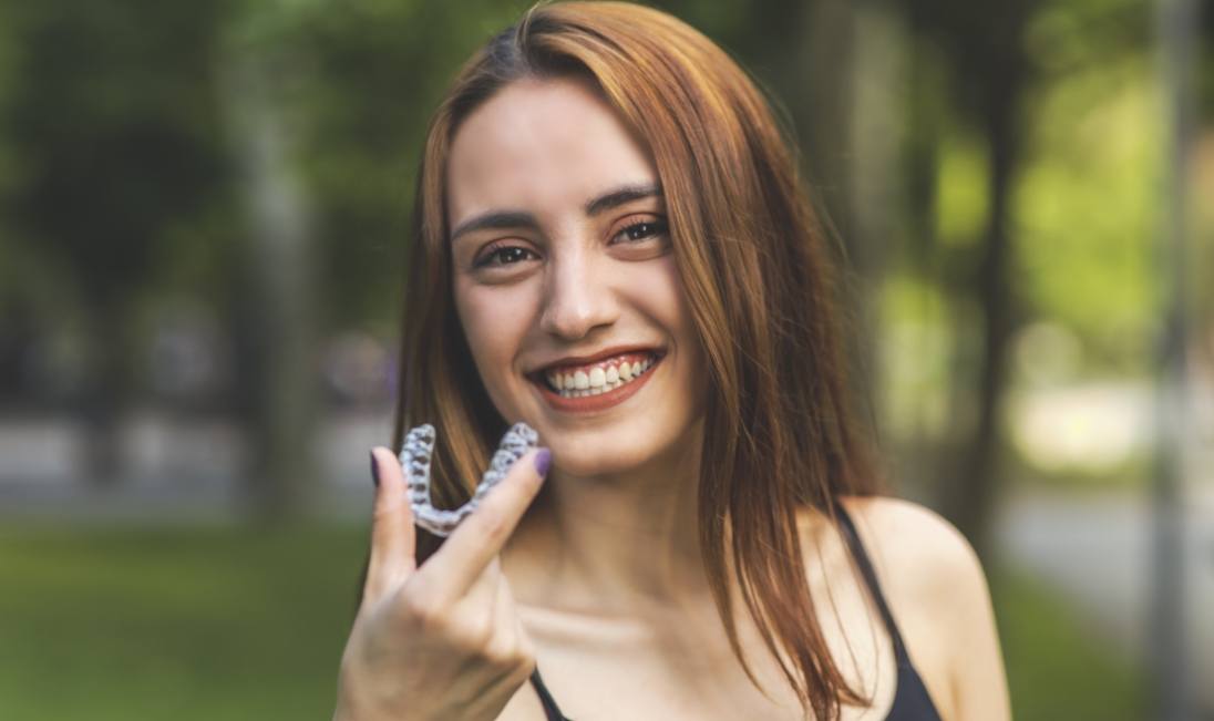 Smiling young woman holding an Invisalign clear aligner outdoors