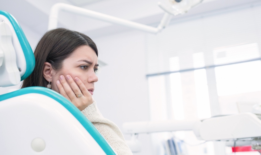 Young woman in dental chair holding the side of her face in pain
