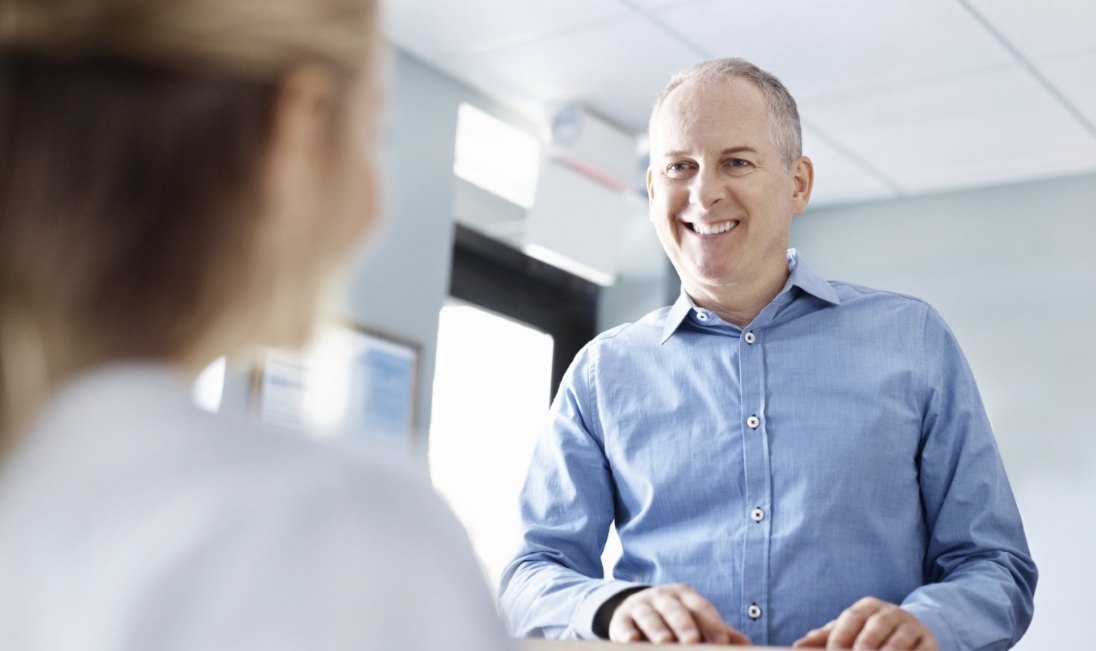 Smiling man in denim shirt talking to dental team member