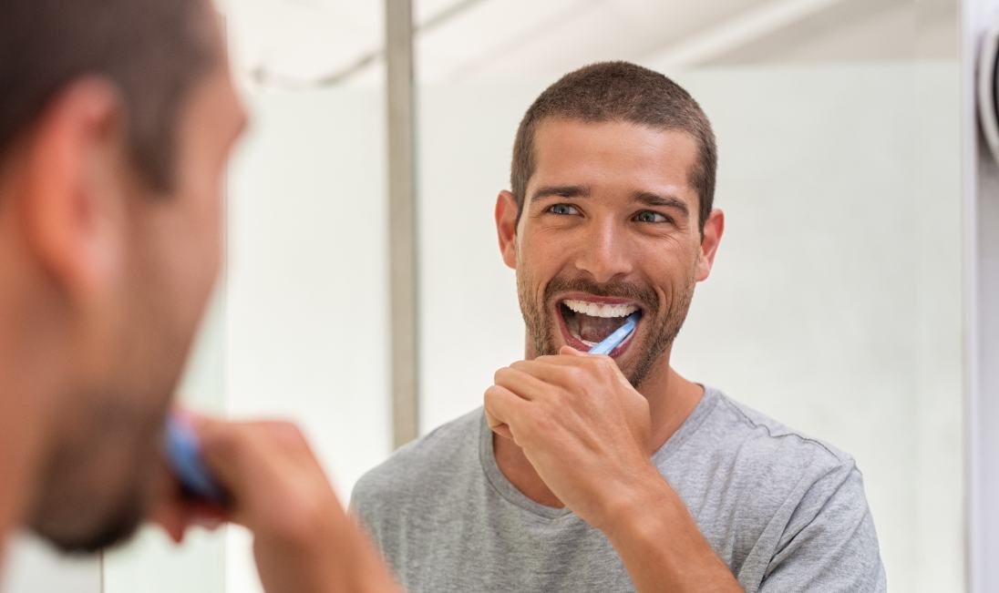 Man smiling while brushing his teeth in front of mirror
