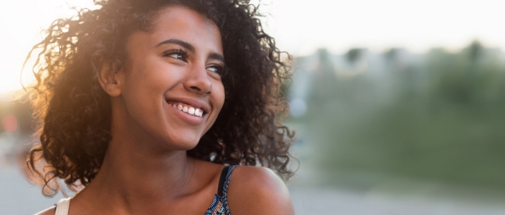 Young woman with curly hair smiling outdoors at sunset