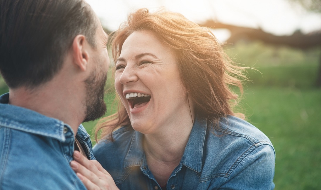 Man and woman laughing together outdoors after replacing missing teeth in Ramsey
