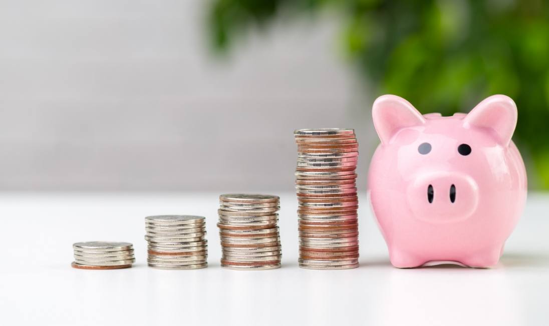 Several stacks of coins next to a pink piggy bank