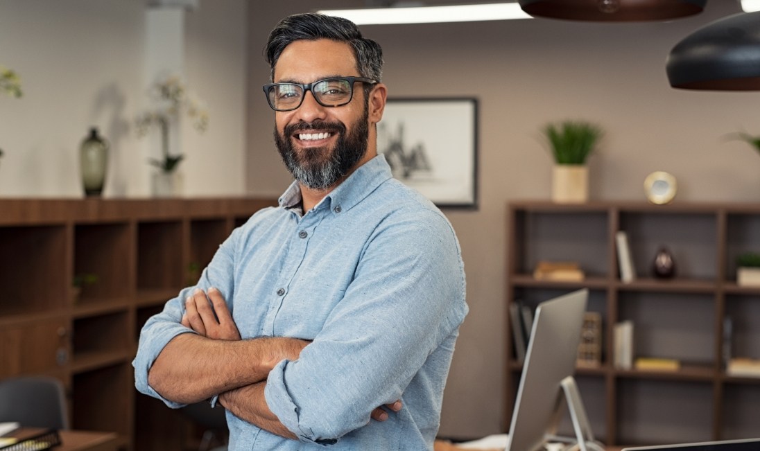 Smiling man in denim shirt standing with arms crossed