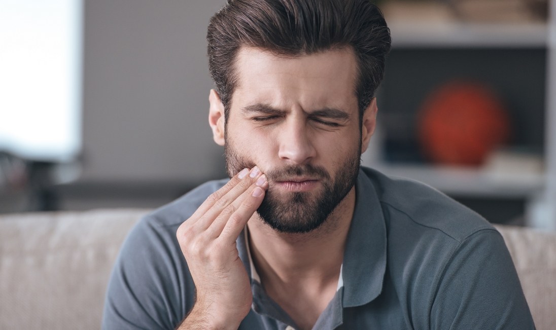Bearded man who needs root canal treatment in Ramsey holding the side of his jaw in pain