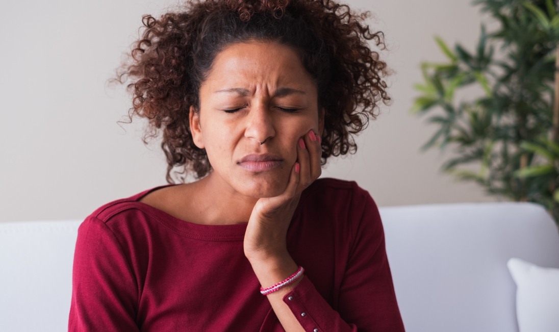 Woman in red shirt holding her face in pain