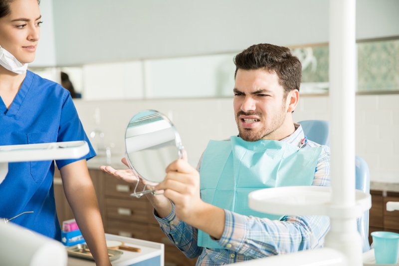 An unhappy man looking at his small teeth in a hand mirror