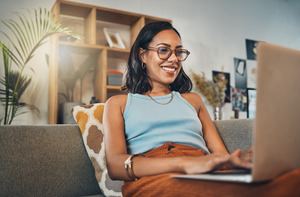 Woman with glasses smiling and looking at a laptop