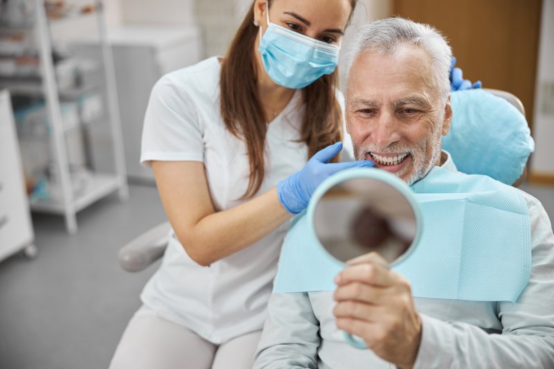 An older man admiring his new dental implant in a hand mirror